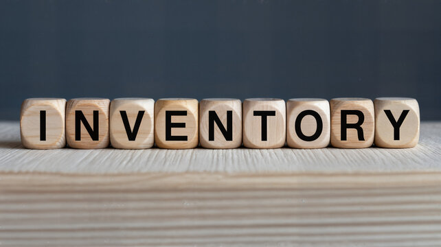 Inventory management concept displayed with wooden blocks spelling inventory on a light wood surface against a dark representing stock and supply chain