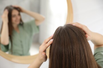 Fototapeta premium Woman using talcum powder as dry shampoo near mirror at home