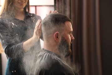 Obraz premium Hairstylist applying talcum powder onto man's hair at salon, closeup