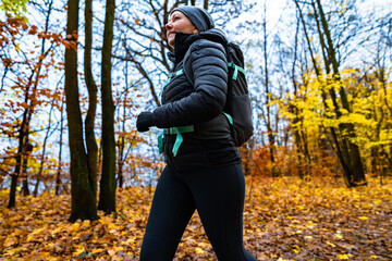 Middle-aged woman training running in forest on autumn day. Side view