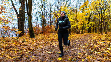 Middle-aged woman training running in forest on autumn day. Front view