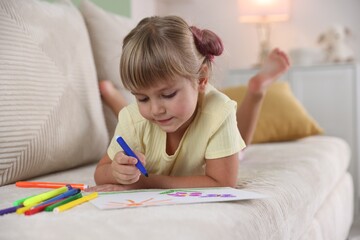 Cute little girl drawing with felt pen on sofa at home
