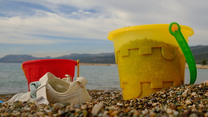 Children's yellow and red bucket and children's shoes on the beach.