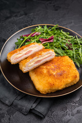 Chicken cordon bleu cutlet with cheese and ham on plate with salad. black background. top view