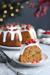 Piece of delicious Christmas cake with icing, cranberries and rosemary on grey textured table against blurred lights, closeup. Bokeh effect