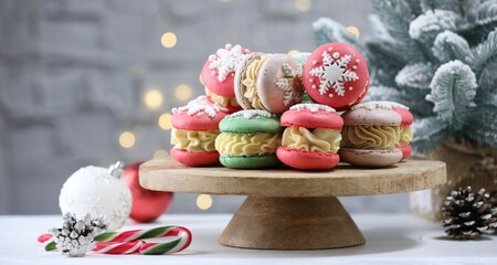 Tasty macarons and Christmas decor on white table against blurred lights, closeup. Space for text