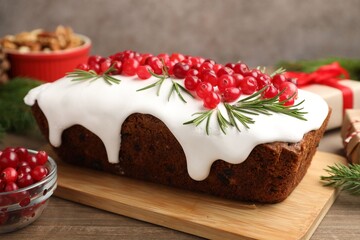 Tasty Christmas cake with icing, cranberries, rosemary and festive decor on wooden table, closeup