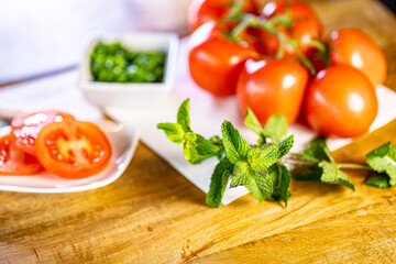 Red fresh tomatoes with mint and basil on wooden table over bokeh background