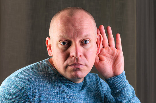Man listening intently with hand cupped behind his ear, close up portrait