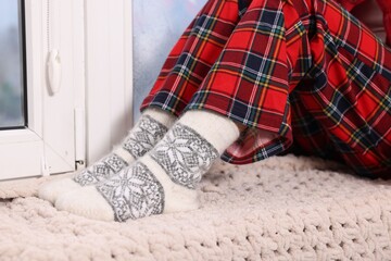 Woman in pajamas sitting on windowsill at home, closeup. Winter season