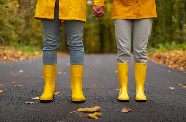 Close-up of a couple holding hands on an autumn road, wearing matching yellow raincoats and boots. Romantic fall walk concept, perfect for Valentine’s Day themes.