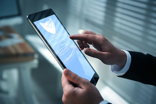 Man entering password on tablet computer, closeup. Username and code boxes and shield on device screen. Cyber security and data protection concept