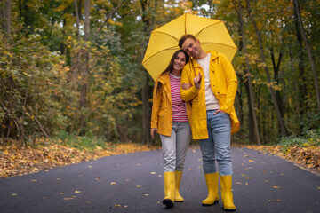 Happy couple celebrating Valentine&rsquo;s Day on an autumn walk, standing close under a yellow umbrella. Romantic fall mood, love, warmth, and togetherness in a scenic forest.