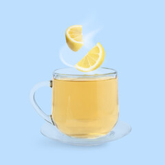 Citrus drink for health boosting. Lemon pieces falling into cup on light blue background. Cold season remedy