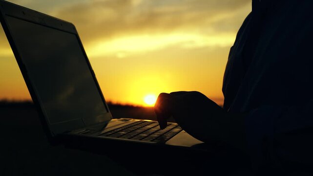 Businessman farmer with laptop working on field, estimating grain harvest. Laptop in hands of businessman outdoors, close-up. Farmer man working on computer, sunset. Agricultural business concept