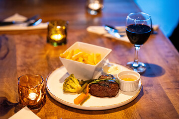 Beef steak meat with fried fryes vegetables and sauce served with red wine and candles