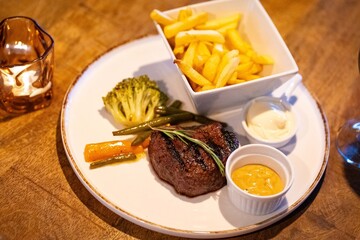 Beef steak meat with fried fryes vegetables and sauce served with red wine and candles