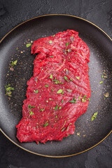 Marinated Flank or Flap steak, raw beef meat with thyme and spices on plate. black background. top view