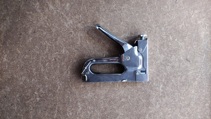 Top view of shiny metal staple gun placed on a brown textured surface, showcasing a common hand tool used for fastening materials.
