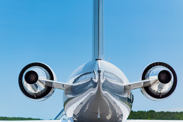 Centered rear view of a private jet showing both engines, tail section, polished surfaces, and clear sky lighting from a straight-on position.