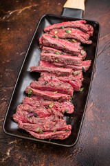 BBQ Grilled Flank beef steak, sliced meat with herbs, brown background. top view