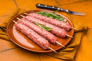 Raw Turkish Urfa kebab skewers on a plate with herbs. orange background. top view