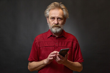 Old man over 60 portrait in studio with smartphone on black background