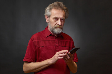Old man over 60 portrait in studio with smartphone on black background