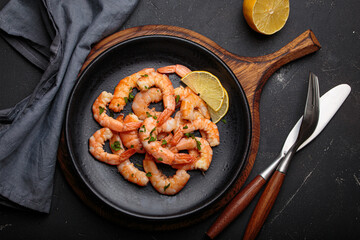 Cooked shrimps prawns arranged on a black plate with lemon wedges and chopped parsley, elegant top view seafood appetizer on dark background