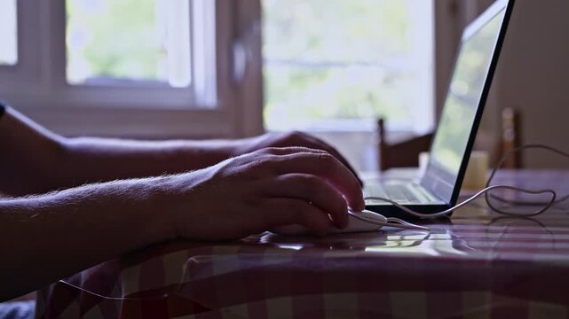 A man cuts his credit card with scissors while sitting at a table with a laptop. This action can symbolize financial difficulties, debt relief, or a fresh start from overwhelming expenses.