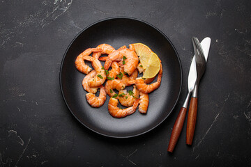 Cooked shrimps prawns arranged on a black plate with lemon wedges and chopped parsley, elegant top view seafood appetizer on dark background