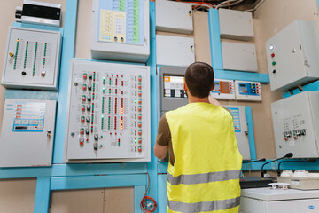 Technician checking control panels with indicator lights in industrial control room
