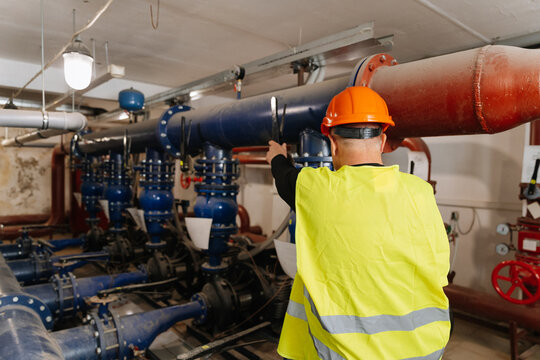 Engineer inspecting large blue industrial pipes and valves, safety vest and hard hat - Powered by Adobe