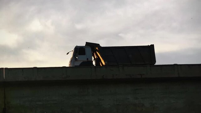 A dump truck moves across a concrete bridge with soft evening light. Suitable for industrialisation themes, construction, logistics, transport infrastructure and heavy vehicle concepts