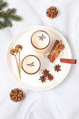 Eggnog with cinnamon, star anise, and nutmeg for Christmas and the winter holidays on a marble table with fir branches. A warming eggnog during the cold season, a festive arrangement for Christmas Eve
