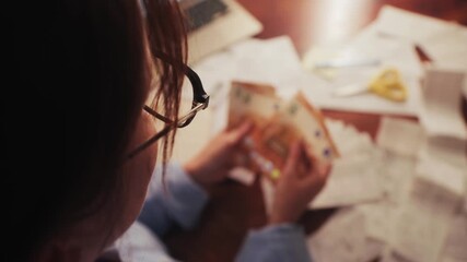 Close up of hands counting euros while sitting at a table. Utility bills and receipts are on the table. The process of calculating a family budget. High quality 4k footage - Powered by Adobe