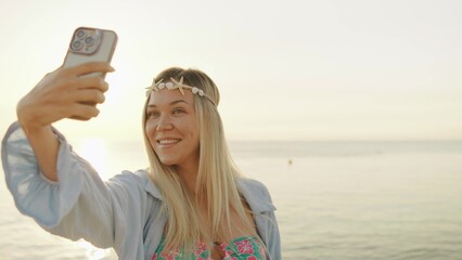 Young woman taking a selfie at sunset by the beach, capturing a joyful moment with warm sunlight illuminating her surroundings