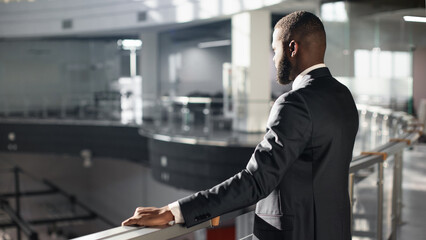 Pensive african american young man in suit entrepreneur standing by railing, experiencing difficulties at work, looking down at business center side view shot, panorama with copy space © Prostock-studio