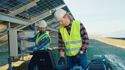 Two technicians working on solar panels at a renewable energy site in the afternoon