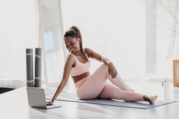 A positive millennial African American woman in sportswear is enjoying her stretching routine at...