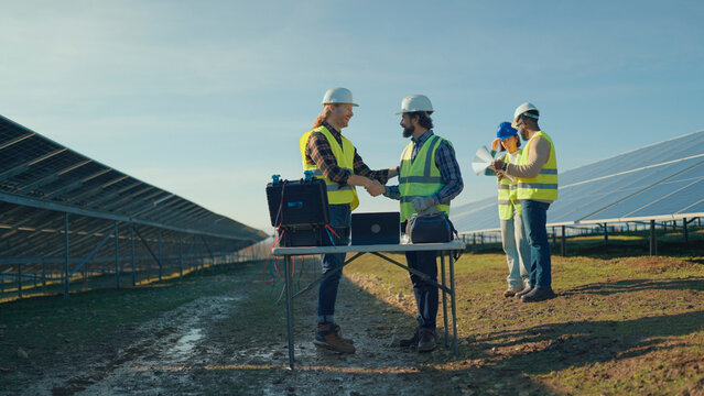 Workers discuss solar energy project progress at a renewable energy site in bright daylight - Powered by Adobe