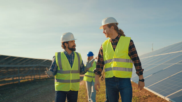 Two men in safety vests discuss solar panel installation during sunny day on construction site