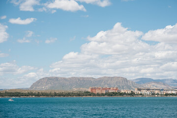 Scenic coastal landscape with mountains, cityscape, and blue ocean under cloudy sky
