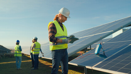 Workers inspect solar panels at a renewable energy site during a clear afternoon in a rural location