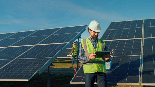Engineer inspects solar panels while using a tablet in a renewable energy field in sunny weather