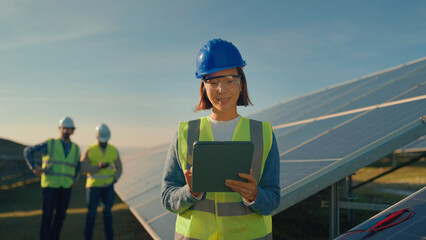 Women in hard hats and safety vests inspect solar panels during a sunny day while managing renewable energy project