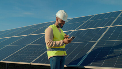 Worker checks smartphone while standing near solar panels in clear weather