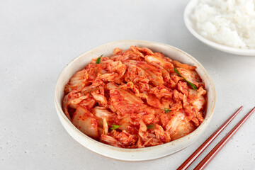 Korean kimchi in ceramic bowl with steamed rice, chopsticks on white background. Fermented food concept.