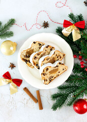 Sliced Christmas stollen with marzipan decorated with fir branches and spices on white background. Top view.