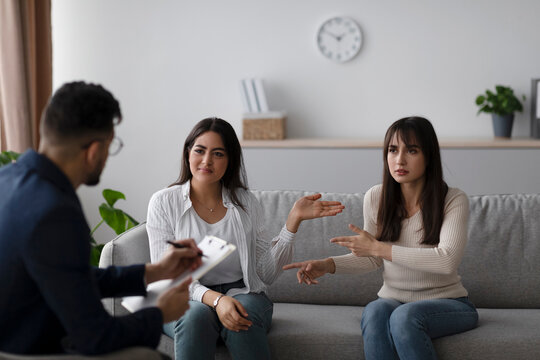 A young arab lesbian couple engages in a heated discussion while sitting on a couch during a counseling session. They are seeking help from a therapist in a modern office environment. - Powered by Adobe